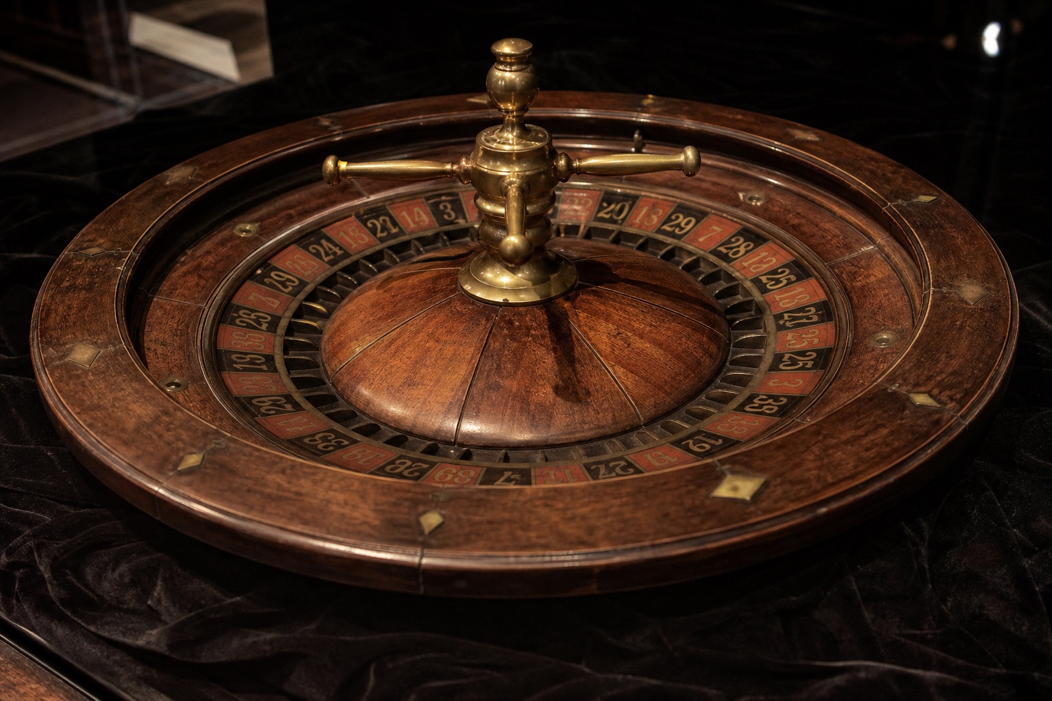 Antique lacquered wooden roulette wheel with worn brass fittings, isolated on dark velvet under a soft spotlight